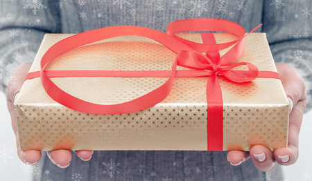 Female hands holding a gift box with a bow and ribbon.