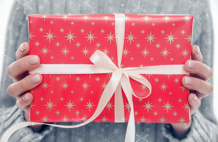 Female hands holding a gift box with a bow and ribbon.