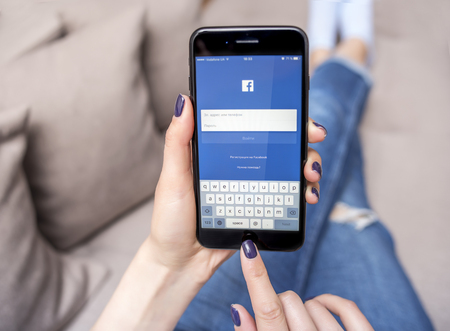 UZHGOROD, UKRAINE - MAY 11, 2017: New black iPhone 7 Plus, with social network Facebook in the hands of the woman sitting on the couch, on May 11, 2017 in Uzhgorod, Ukraine.のeditorial素材