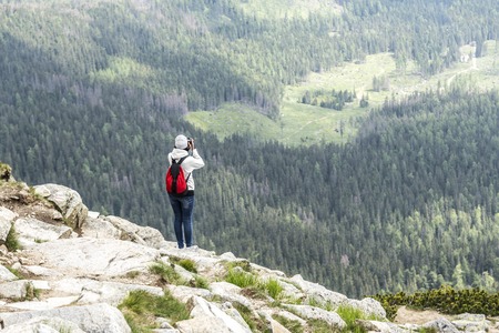 Woman photographer taking photo at mountain peak.の写真素材