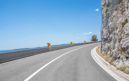Asphalt highway in a sunny day outside the city passing through the cliff next to the sea.