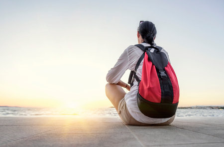 A young woman sits relaxed and looks at the sunset on the seashore.の写真素材