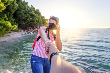View from the first person of a man who holds a girls hand with a photo camera on the seashore.