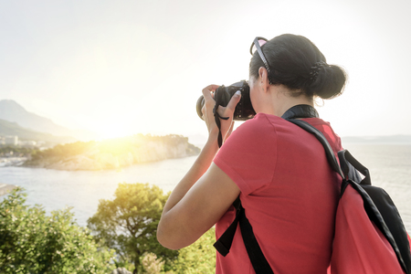 Woman with a camera photographing the sunset on the sea coast.の写真素材