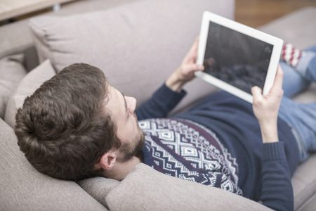 A man sitting on the couch uses a tablet PC. Back view.の写真素材