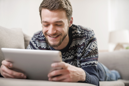 Young man with tablet computer in their hands, on the couch at home.の写真素材