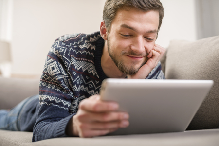 Young man with tablet computer in their hands, on the couch at home.の写真素材