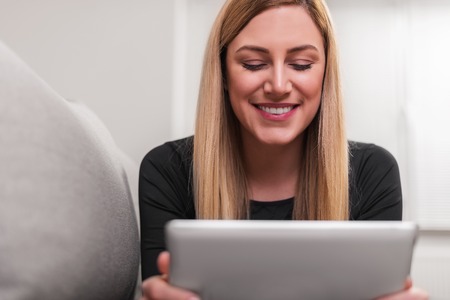 Attractive woman using a tablet pc while lying on the couch at home.の写真素材