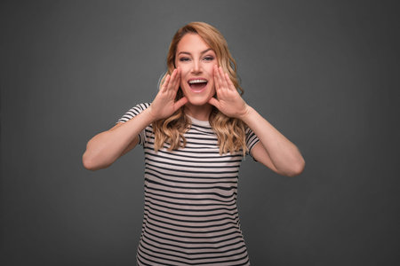 A woman screams with her arms folded. Beautiful young blonde on grey background.