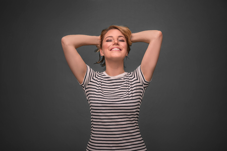 Young woman relaxing with hands behind head on gray background.の写真素材