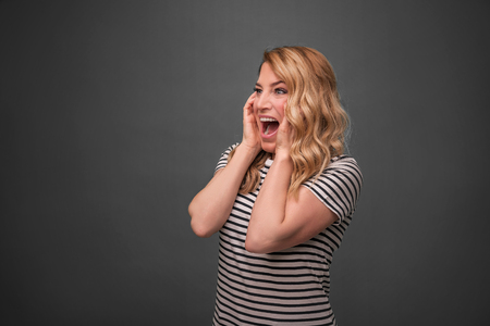 Emotional blonde screams. Frightened woman screaming straining standing on a gray background.の写真素材