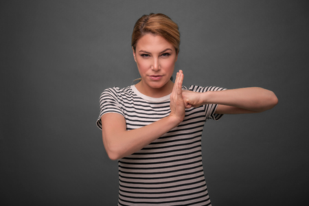 Beautiful woman shows a lock sign, resting her fist in the palm on gray background.の写真素材