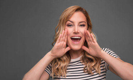A woman screams with her arms folded. Beautiful young blonde on grey background.