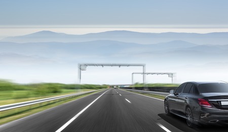 The car drives fast on the highway against the backdrop of a mountain range.の写真素材