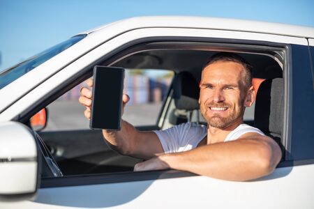 An attractive man in a car shows a smartphone.の写真素材