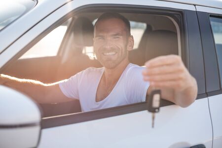 A man in a white car shows a key.の写真素材