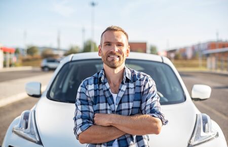 An attractive young man stands near a car.の写真素材
