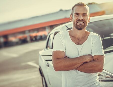 An attractive man is standing against a white car.の写真素材