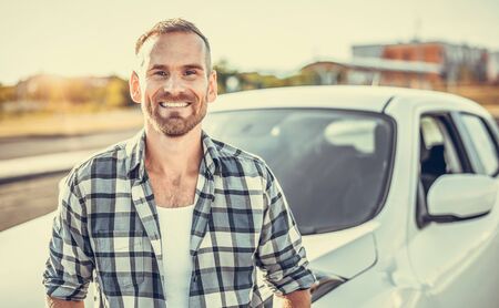 An attractive young man stands near a car.の写真素材