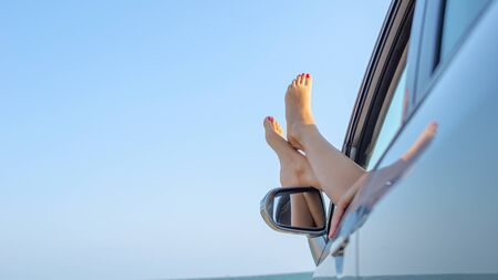 Female legs out of a car window on a background of a sea landscape.の写真素材