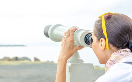 Woman tourist looks through a spyglass in the open.