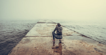 A photographer on a concrete pier takes a picture of a foggy sea.