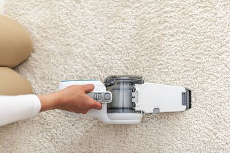Woman vacuuming furniture in a house with a hand-held portable vacuum cleaner.の写真素材