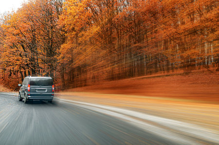 The minivan is driving along the road against the background of the autumn forest. Blur effect.の写真素材