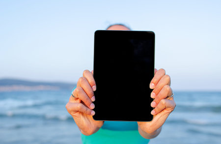 Woman with a tablet in hands on the background of the sea on a warm day.