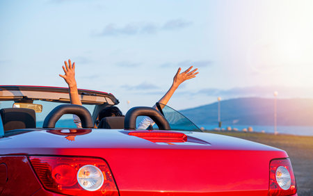 Woman in red car with open roof at background of sea water.の写真素材