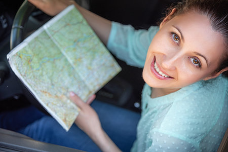 Young woman driver with a paper map in her hands.