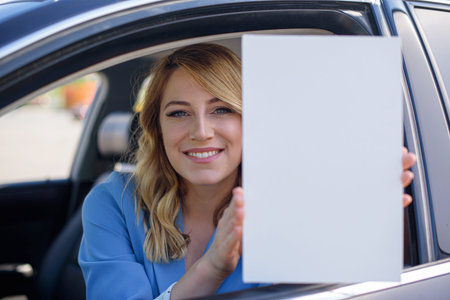 Young woman holding a blank sheet of paper in front of a car