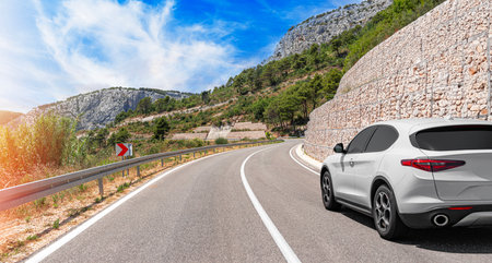 A white car drives along the highway against the backdrop of mountains on a sunny day.の写真素材