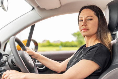 A young woman with long brown hair, wearing a black shirt, is sitting in the drivers seat of a car