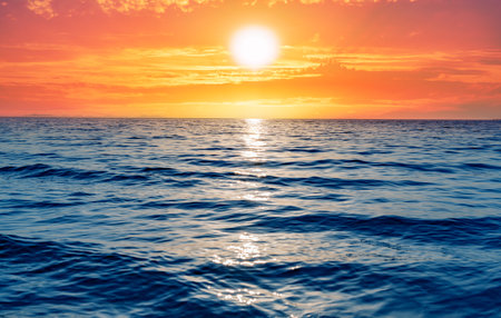 A serene ocean scene captures the golden sun setting over the horizonの写真素材