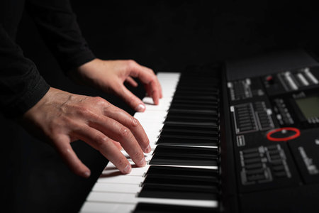 A pair of hands with long slender fingers gently presses down on the white keys of a digital piano