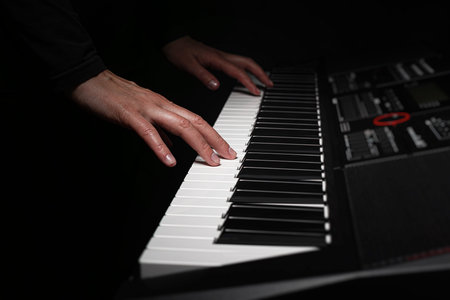 A pair of hands with long slender fingers gently presses down on the white keys of a digital piano