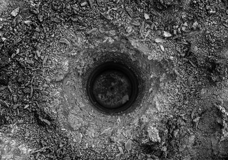 Freshly drilled hole in the rough soil, showing detailed texture of earth and gravel around the circular opening.の写真素材