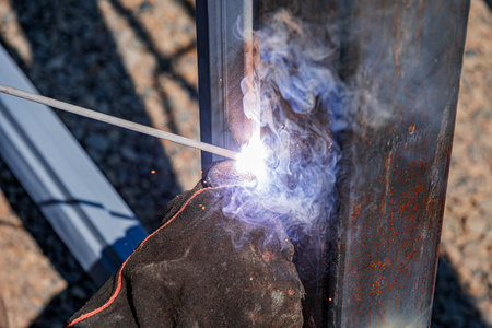 A worker welding two metal beams together outdoors