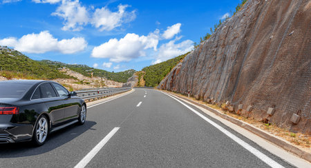 A black sedan drives along a winding mountain road
