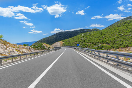 An empty, winding road curves through a mountainous landscapeの写真素材