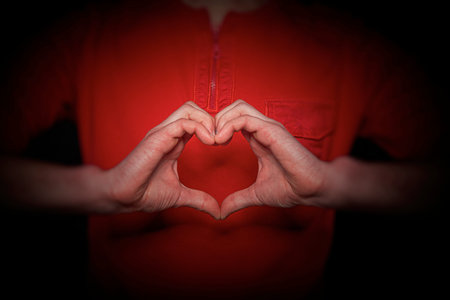 A person wearing a red shirt forming a heart shape with their hands