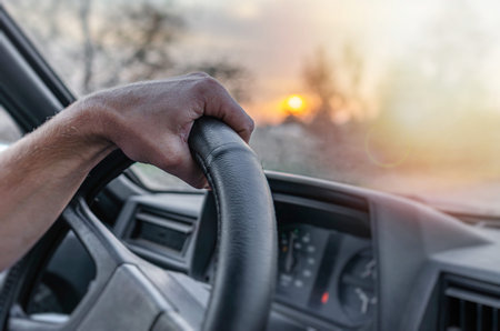 Inside a car shows a persons hand gripping the black steering wheel