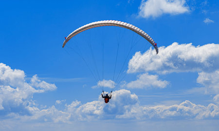 A lone paraglider with an orange wing soars high above the ground against a brilliant blue sky