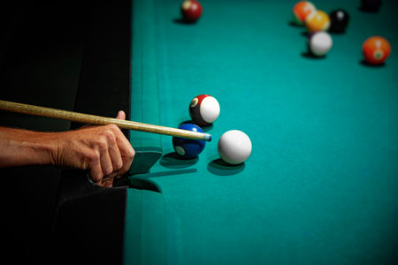 A male players hand aiming a wooden cue stick at the white ball near the corner pocket during a game...