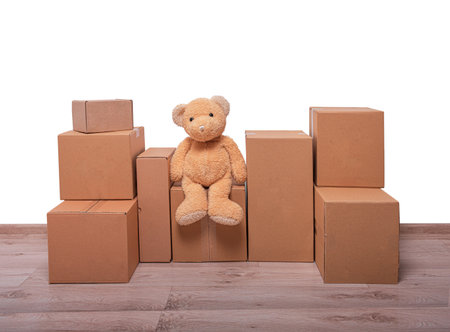 A fluffy, brown toy bear is sitting among a large arrangement of stacked, plain cardboard moving boxesの写真素材