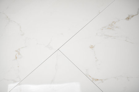 A white marble tile surface with gold and grey veining and thin grout lines.の写真素材