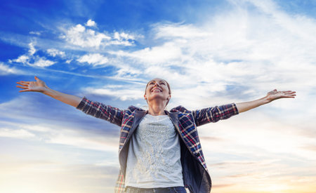 A joyful woman stands with her arms wide open against a beautiful blue sky.