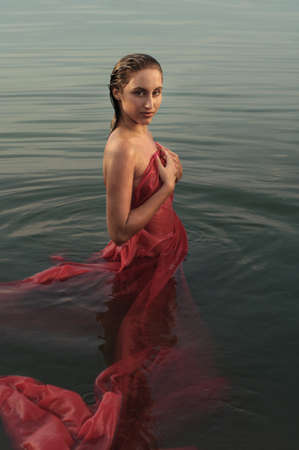  beautiful girl in red clothes posing in the water at sunsetの写真素材