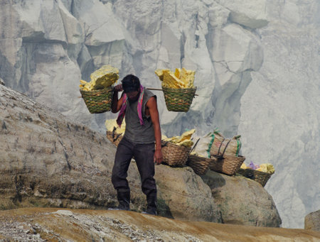 IJEN VOLCANO, INDONESIA - JAN 10:Worker carries sulfur inside crater on January 10, 2011 in Ijen Volcano, Indonesia. He carries the load of around 60kg to the top of the crater and then 3km down. のeditorial素材